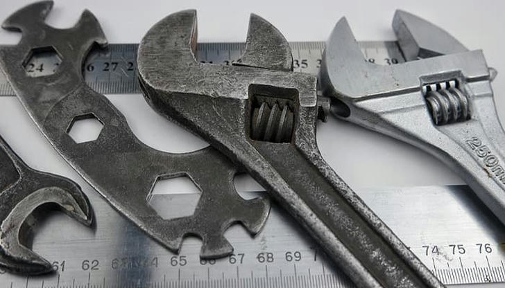 Which tool is adjustable for gripping nuts and bolts of different sizes?