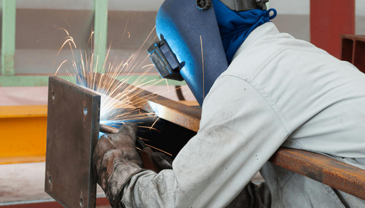 Why should synthetic clothing be avoided while welding?
