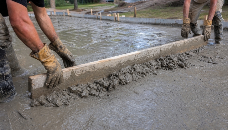 What long, perfectly straight wood or aluminum tool is pulled in a sawing motion by two people to level freshly poured wet mud?