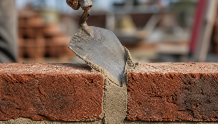 What small, triangular steel shovel hand tool is essential for mixing wet mortar blocks and scraping clay containers clean?